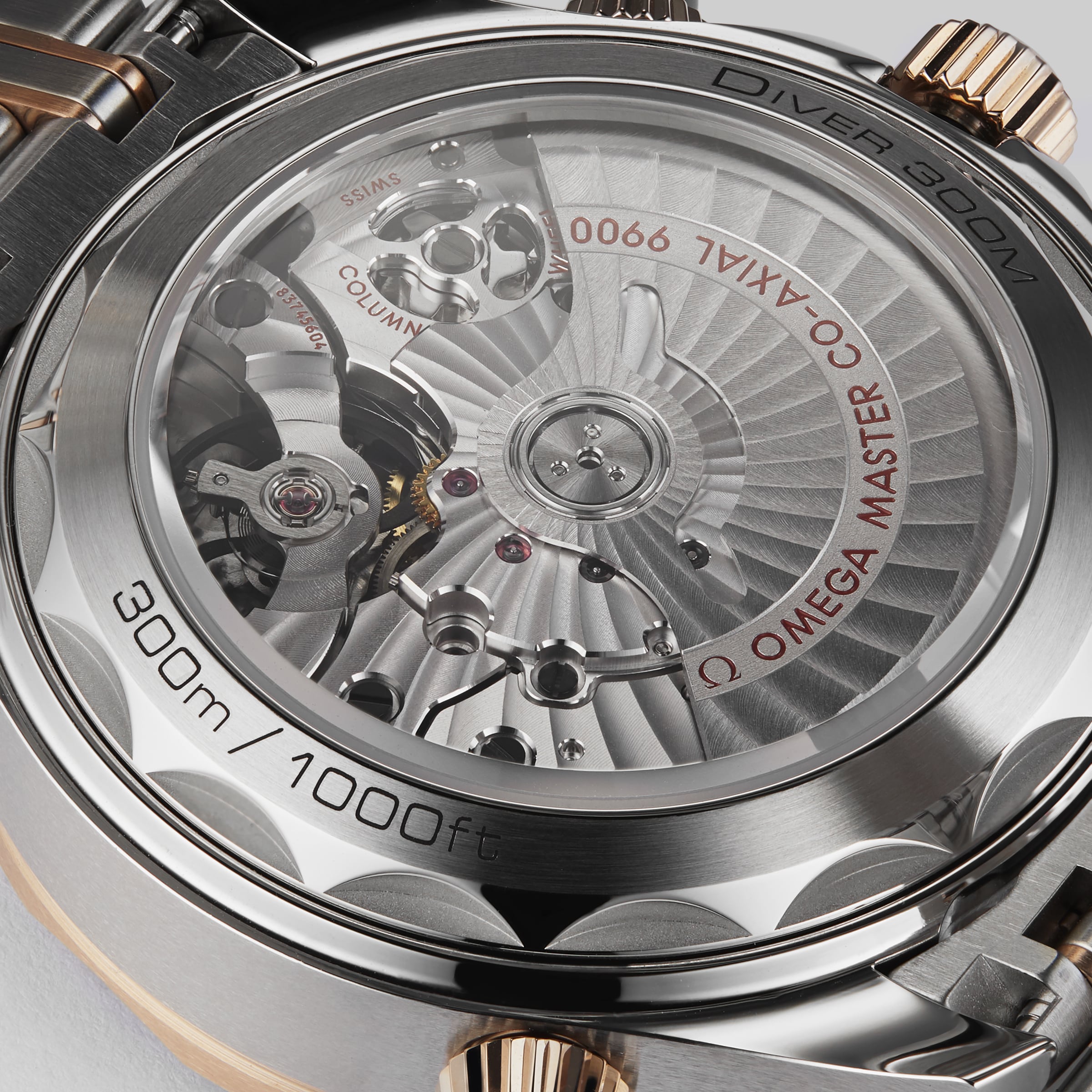 Close-up of the OMEGA Seamaster Diver 300M’s back reveals its mechanical movement, rotor, and engravings like 300m/1000ft, Master Chronometer, and Co-Axial 9900 in luxurious 18K Sedna™ gold.