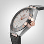 The OMEGA Constellation wristwatch, with a textured silver dial, rose gold Roman numerals, and black leather strap, features a Master Chronometer 8900 movement and is photographed on a light gray background.