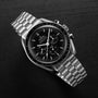 The OMEGA Speedmaster Moonwatch Professional, a stainless steel chronograph with a black dial, is showcased on a dark wooden surface.