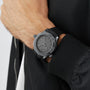 A person wearing an OMEGA Seamaster Diver 300M Black Black Edition watch with a patterned dial and black strap, dressed in a black jacket with a visible zipper.