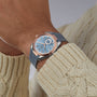 Someone wearing an OMEGA Seamaster Aqua Terra 150M with a blue strap and textured dial in Sedna™ gold, paired with a cream cable-knit sweater.