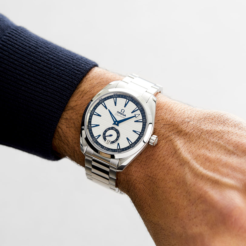 An individual wearing an OMEGA Seamaster Aqua Terra 150M wristwatch with a white dial and blue accents, reflecting maritime heritage, on their left wrist.