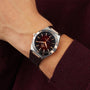 A person in a burgundy sweater showcases the OMEGA Constellation wristwatch, featuring a brown dial, gold hour markers, dark leather strap, and the precise 8900 calibre movement.
