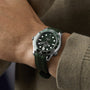 A person wears a green OMEGA Seamaster Diver 300M with a matching green rubber strap, visible over the sleeve of a green sweater.