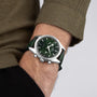 A person wearing a green sweater and the OMEGA Speedmaster 57 wristwatch, which has a stainless steel case, silver bezel, and chronograph functions.