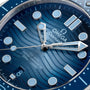 Close-up of the OMEGA Seamaster Diver 300M Summer Blue watch face, showcasing a wave-pattern dial, silver hour markers and hands, date window at 6 oclock, 300m / 1000ft text, and Master Chronometer certification.