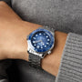 Wearing an OMEGA Seamaster Diver 300M Summer Blue with a metal link band, this person perfectly matches the stylish watch and its blue dial with a grey long-sleeve sweater.