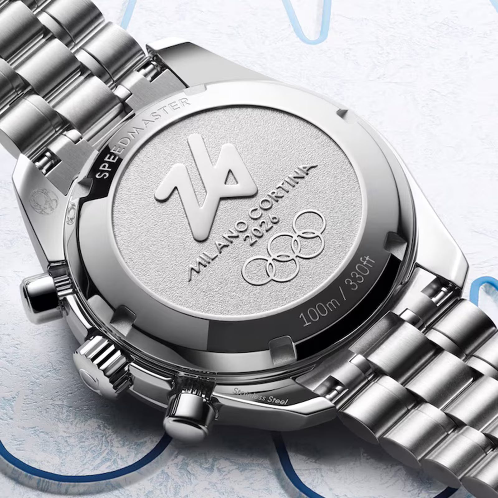Close-up of a silver watch with 'Milano Cortina' branding on a light blue background