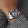 A close-up of a wrist wearing the Raymond Weil Freelancer Calibre RW1212 Automatic, featuring a silver case, blue dial with open-heart mechanism, and paired with a grey knitted sweater—perfect for an urban personality.