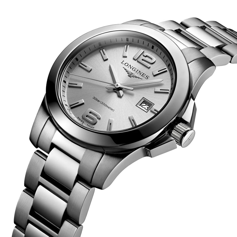 The Longines Conquest watch features a stainless steel design, silver dial, metal bracelet, date at 3 o’clock, and luminous hands and markers—offering performance elegance and timeless style.