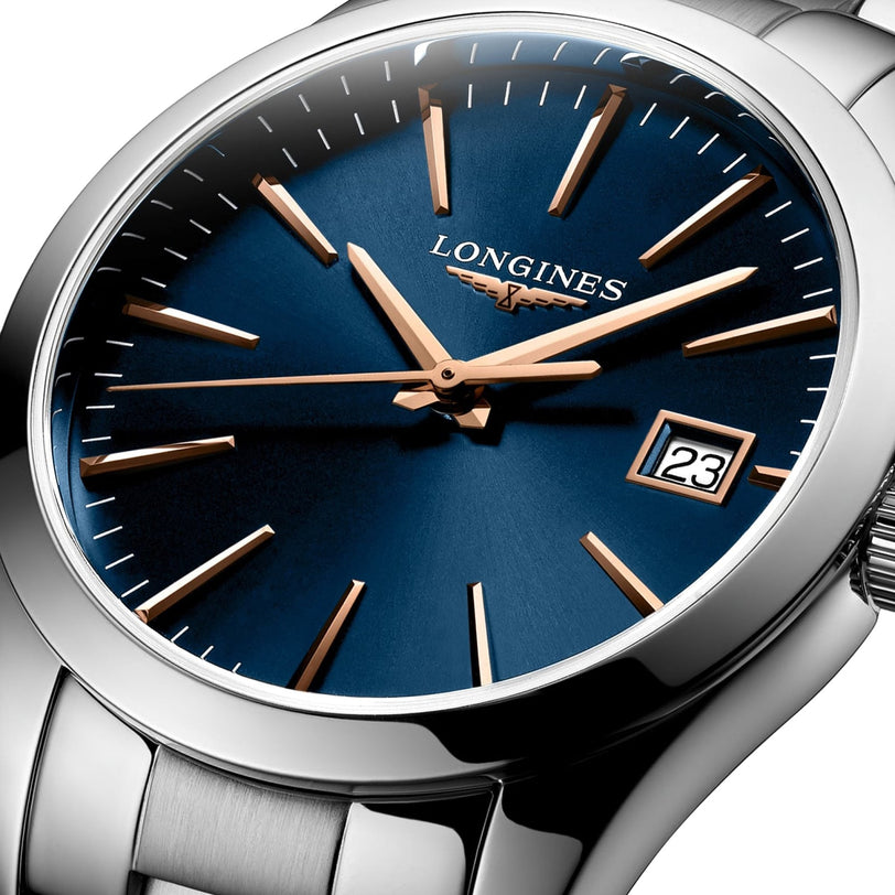 Close-up of a Longines Conquest Classic wristwatch featuring a blue dial, gold hour markers and hands, date display at 3 o’clock, stainless steel case, and silver metal bracelet.