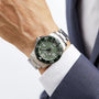 A person in a navy suit and white shirt wears a Longines HydroConquest diving watch with a silver metal band, green face, and white indices.