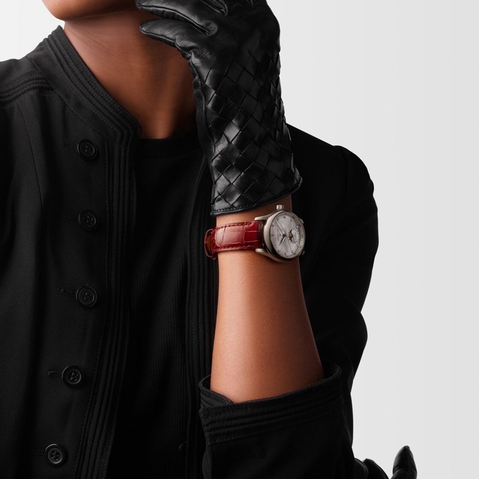 A person in a black glove and jacket showcases the Longines Master Collection Moonphase watch, featuring a silver case, brown leather strap, and elegant moonphase display, set against a plain light background.