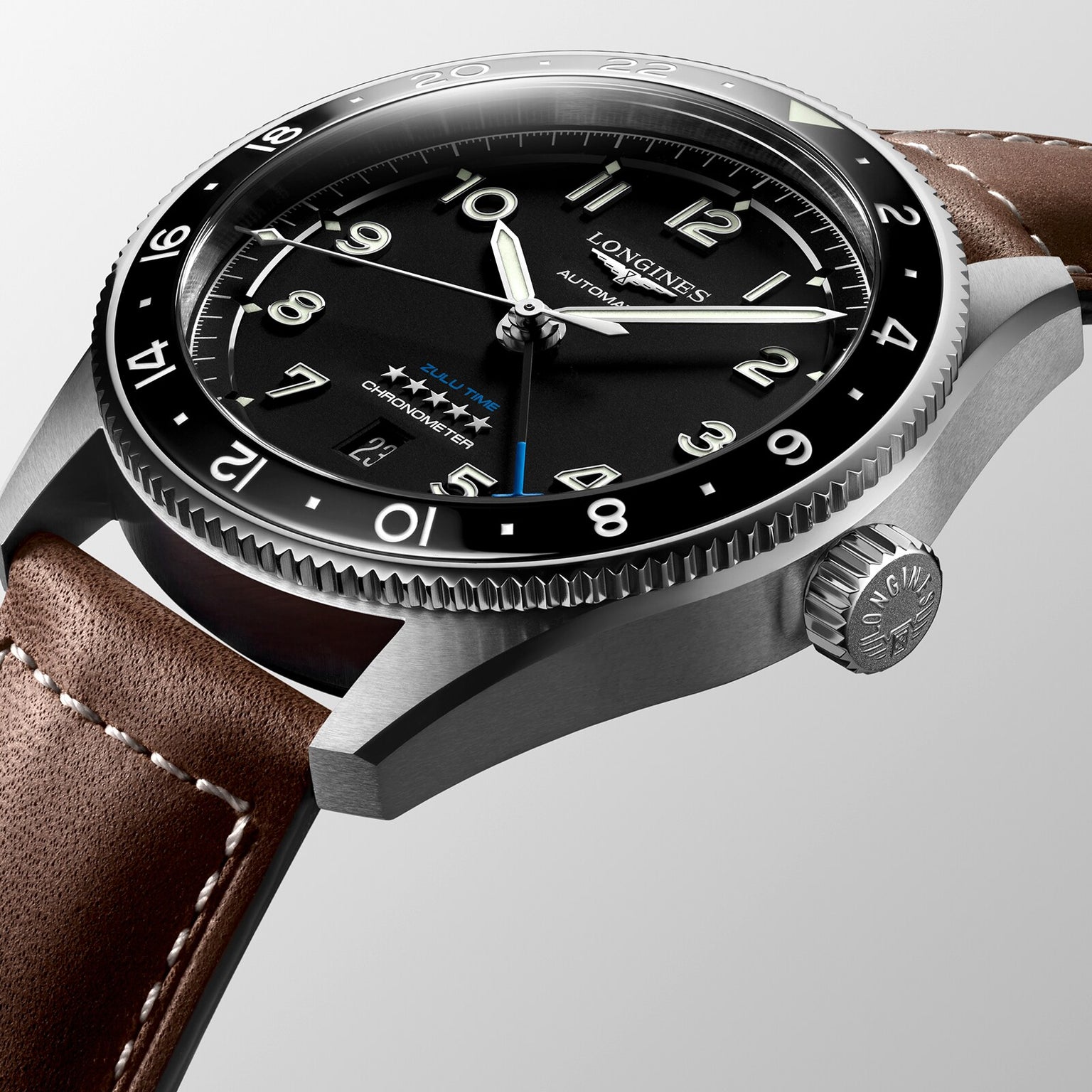 Close-up of the Longines Spirit Zulu Time automatic watch featuring a stainless steel case, black dial, silver hands, date window, brown leather strap, and textured crown.
