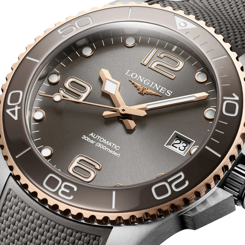 Close-up of a Longines HydroConquest wristwatch featuring a gray dial, gold accents, date display, textured strap, Swiss Super-LumiNova, and 300m water resistance.