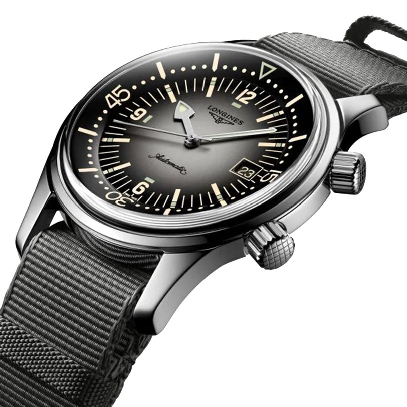 A close-up of the Longines Legend Diver watch, showcasing its L888 calibre movement, black dial with luminous markers, dual crowns, and a green fabric strap.