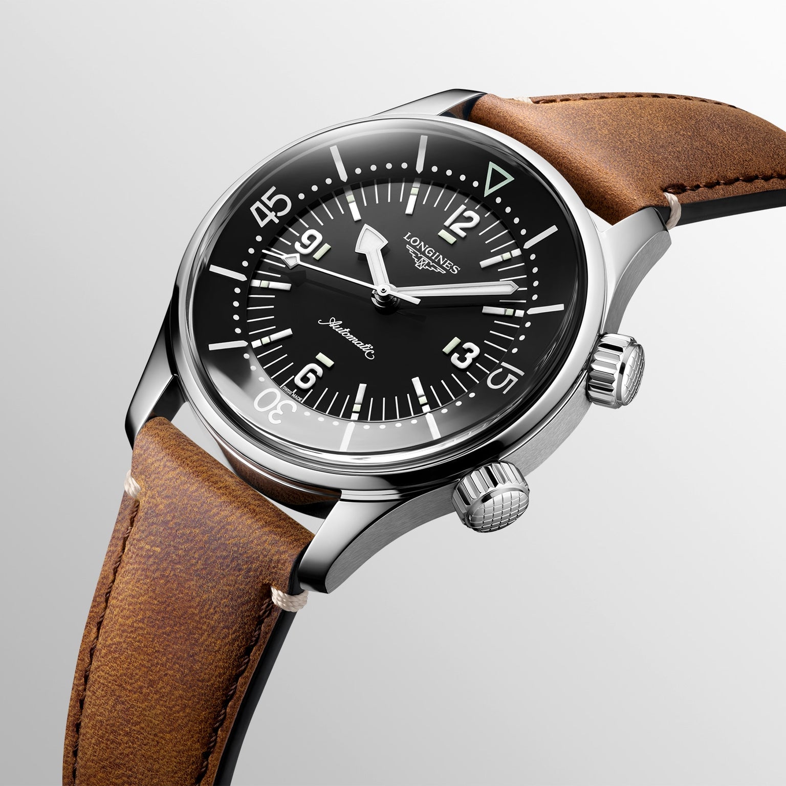 The Longines Legend Diver showcases automatic movement, a black dial with white markers, a rotating bezel, and a brown leather strap—vintage-inspired and elegantly presented at an angle on a light background.