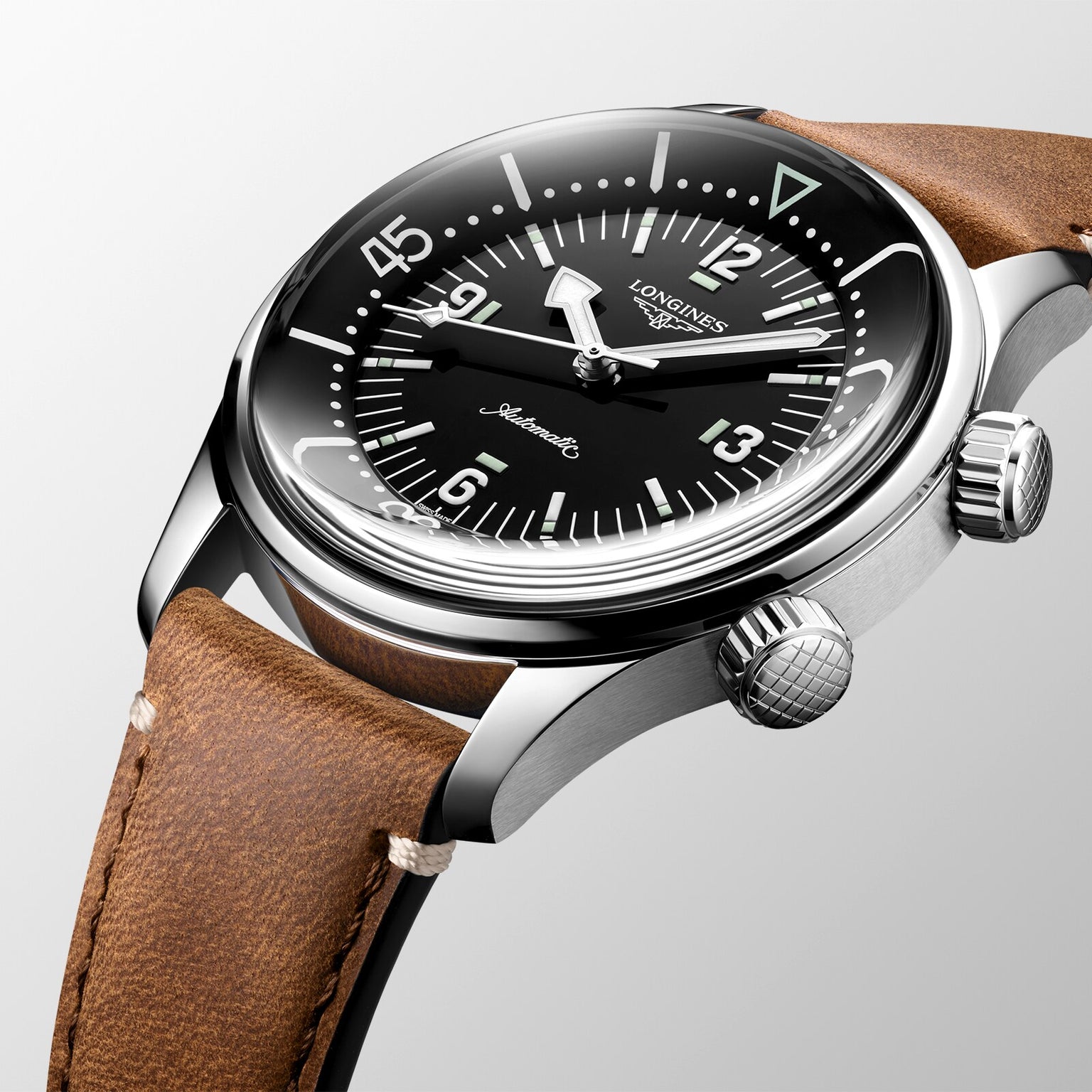 A close-up of the Longines Legend Diver, a vintage-inspired watch with automatic movement, black dial, white markers, dual crowns, and a brown leather strap.