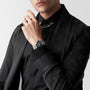 A person in a black shirt and blazer with a silver chain necklace holds their hand near their face, showcasing the Longines HydroConquest GMT diving watch with a stainless steel case.