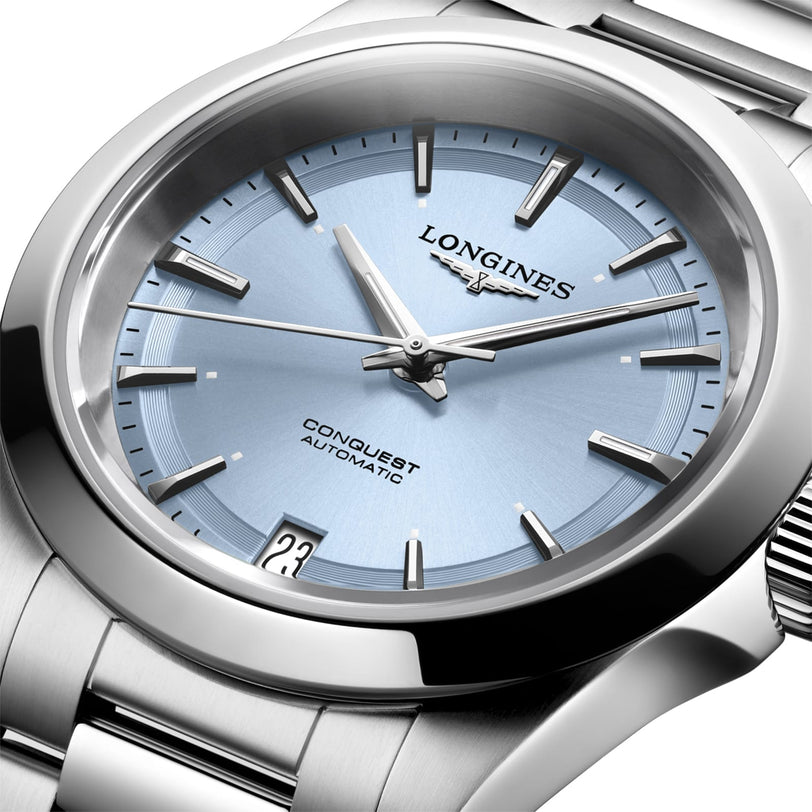Close-up of the Longines Conquest, showcasing its automatic movement, light blue dial, silver hands and markers, date at 6 oclock, and stainless steel bracelet.