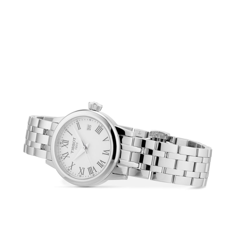 The Tissot Classic Dream, a silver wristwatch with metal link band, white dial, Roman numeral hour markers, and date window, is artfully angled on a white background—an elegant showcase of Swiss quartz style.