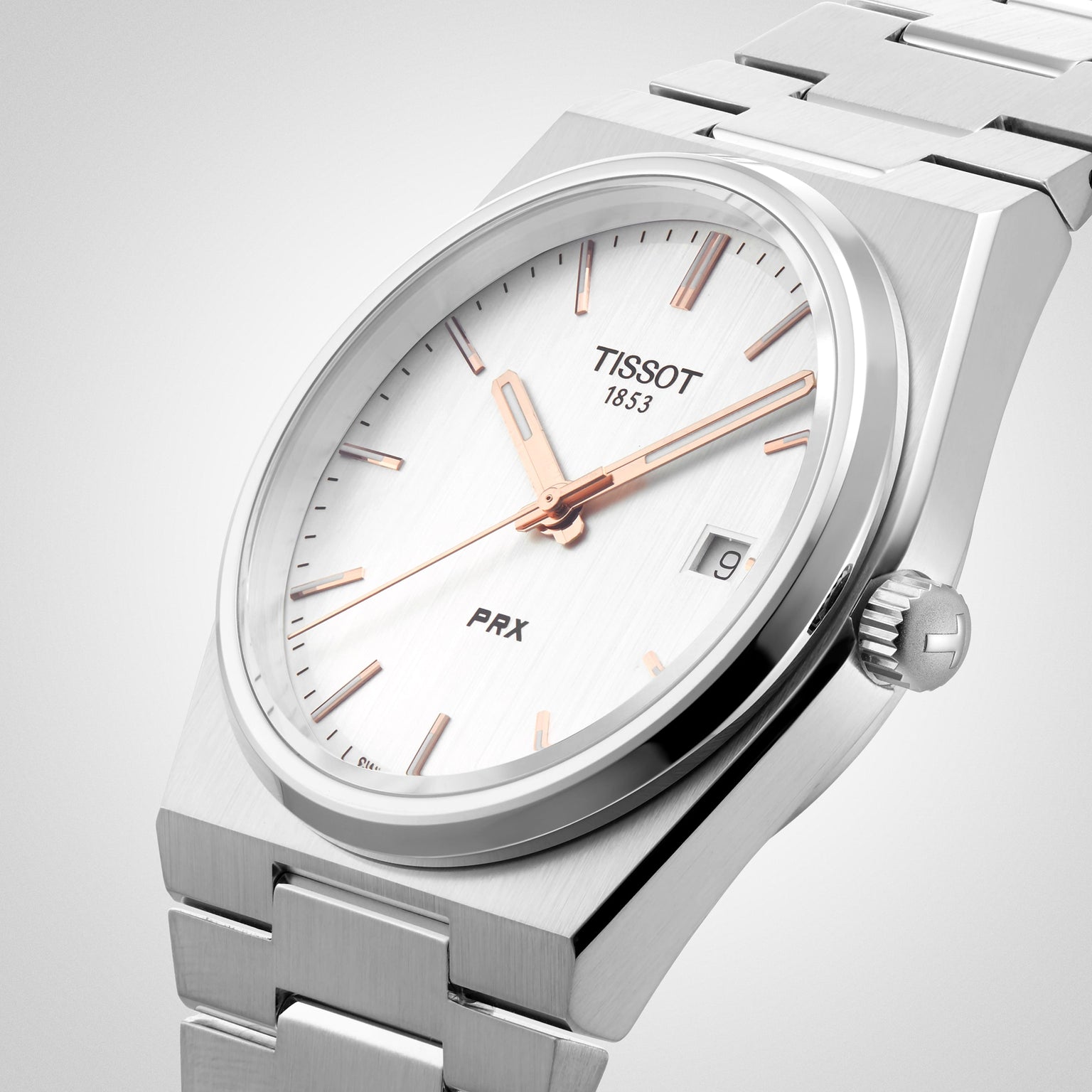 The Tissot PRX is a silver wristwatch with a white dial, rose gold markers and hands, date at 3 o’clock, stainless steel bracelet, and Swiss quartz movement inspired by 1970s design.
