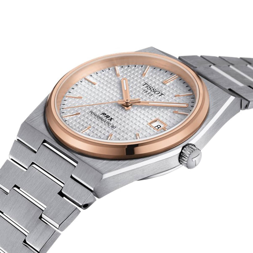 The Tissot PRX Powermatic 80 wristwatch gleams on its stainless steel bracelet, featuring a textured white dial, gold bezel, and date display—exemplifying the refined design of Tissot timepieces.