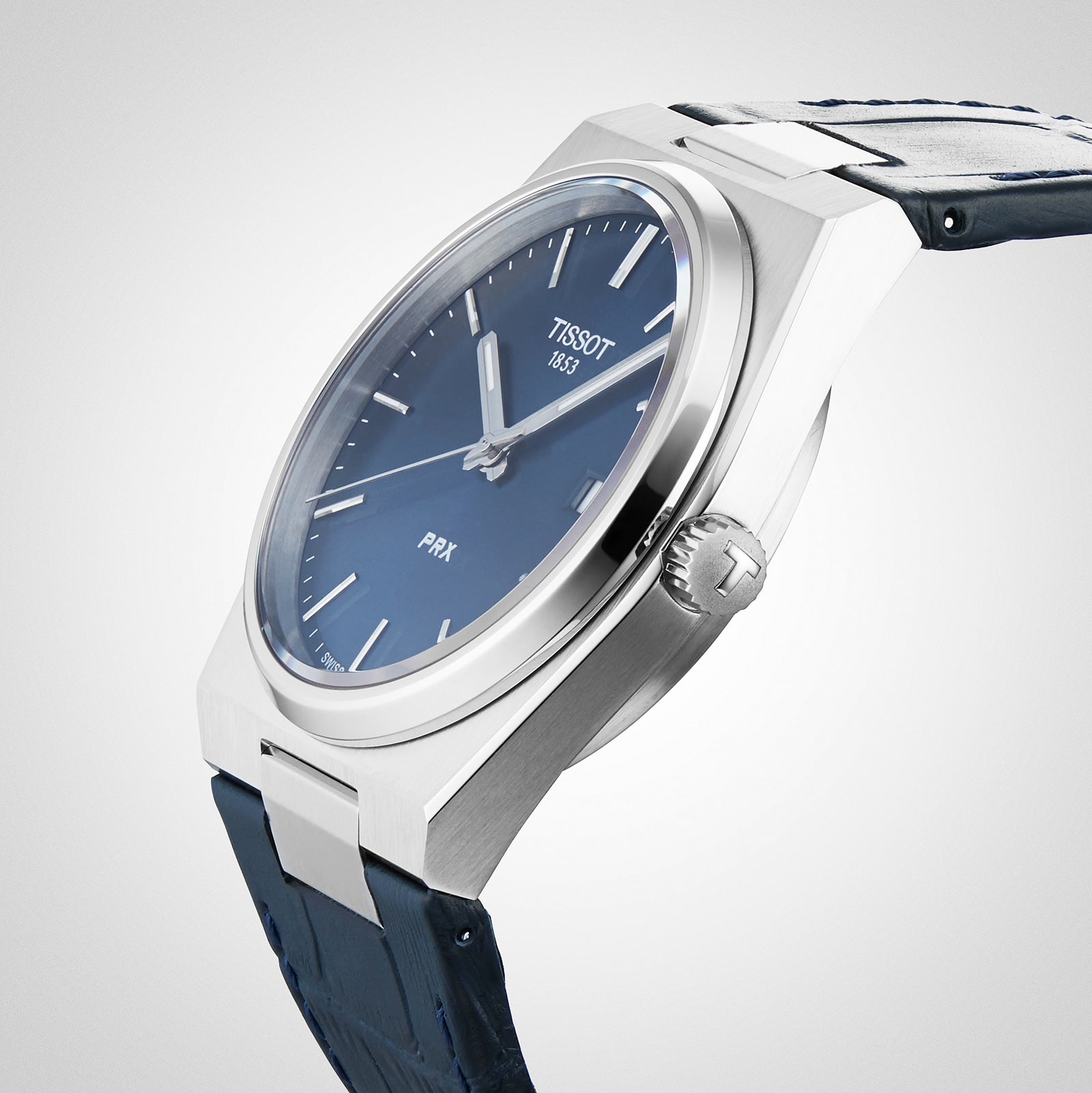A close-up of the Tissot PRX wristwatch, featuring a 1970s-inspired design, blue dial, silver markers, textured blue leather strap, and precise Swiss quartz movement.