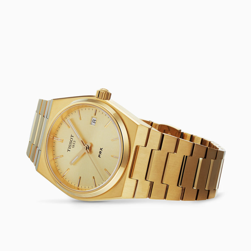 The Tissot PRX is a gold wristwatch with a metal bracelet, gold dial, baton hour markers, and date display—an elegant Swiss-made luxury watch with quartz movement shown against a white background.