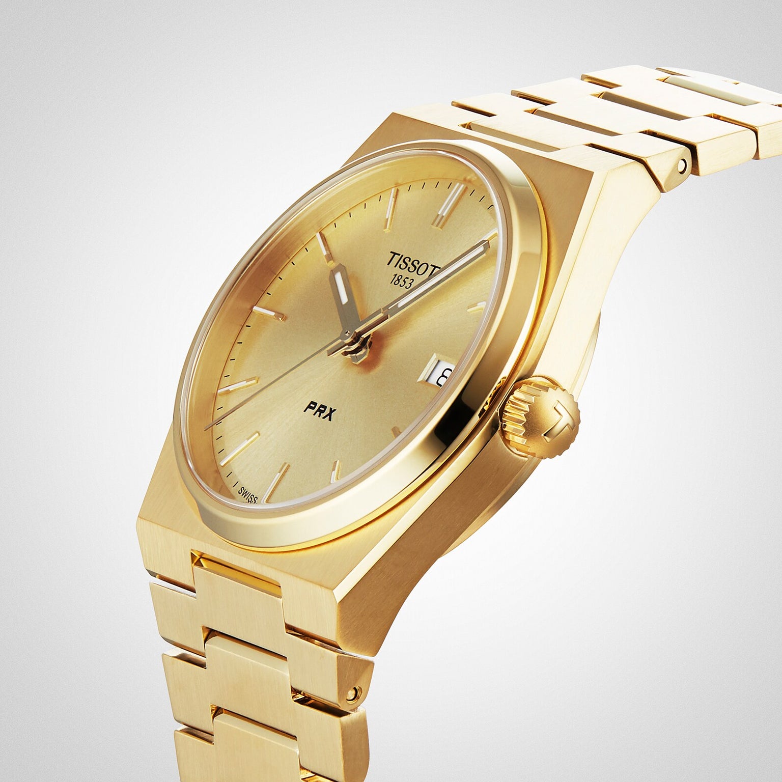 The Tissot PRX gold luxury watch features a metal bracelet, Swiss quartz movement, date display at 3 o’clock, and a minimalist design, shown on a light background.