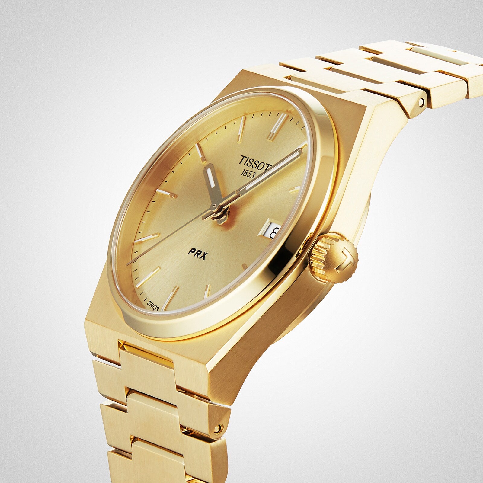 The Tissot PRX gold luxury watch features a metal bracelet, Swiss quartz movement, date display at 3 o’clock, and a minimalist design, shown on a light background.