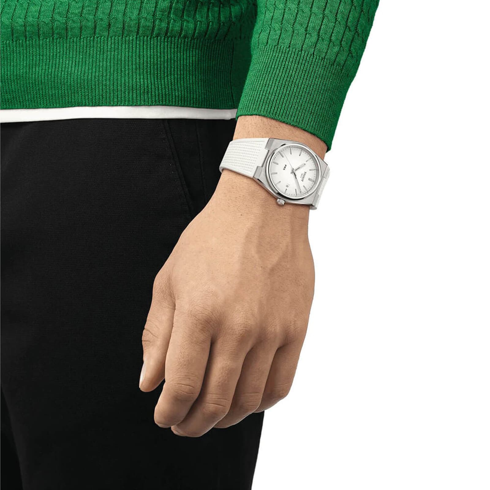 A person in a green sweater and black pants completes their vintage look with a Tissot PRX 40mm watch featuring a white face, worn on their left wrist.