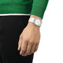 A person in a green sweater and black pants completes their vintage look with a Tissot PRX 40mm watch featuring a white face, worn on their left wrist.