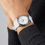 A person in a black ribbed sweater showcases a Tissot PRX wristwatch with a silver case, white strap, and vintage-style 40mm face on their left wrist.