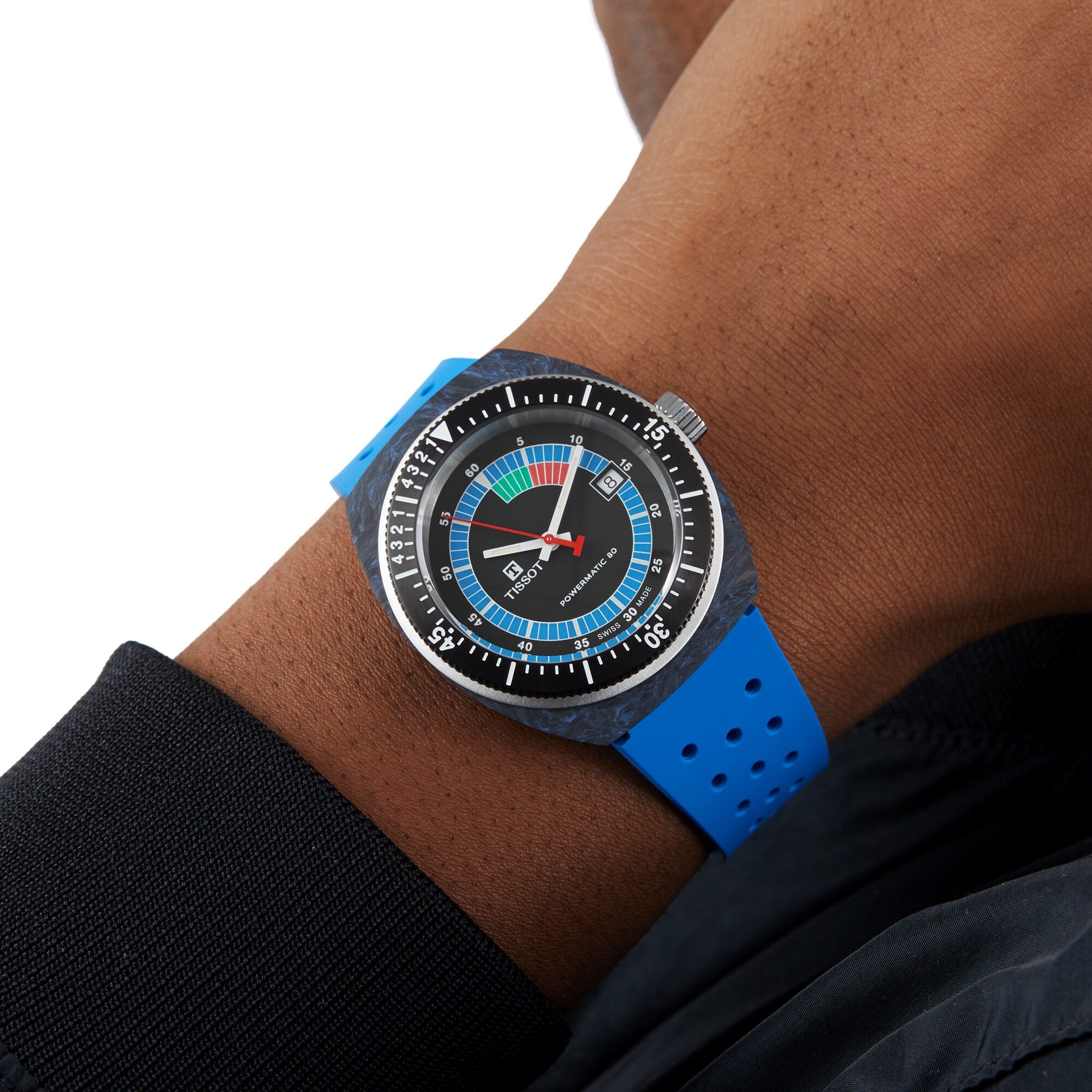 A person wearing the Tissot Sideral S Powermatic 80, a blue and black analog wristwatch featuring a colorful dial and a blue perforated strap.
