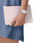 A person in a blue dress holds a beige clutch and wears the Tissot PRX silver wristwatch on their left hand.