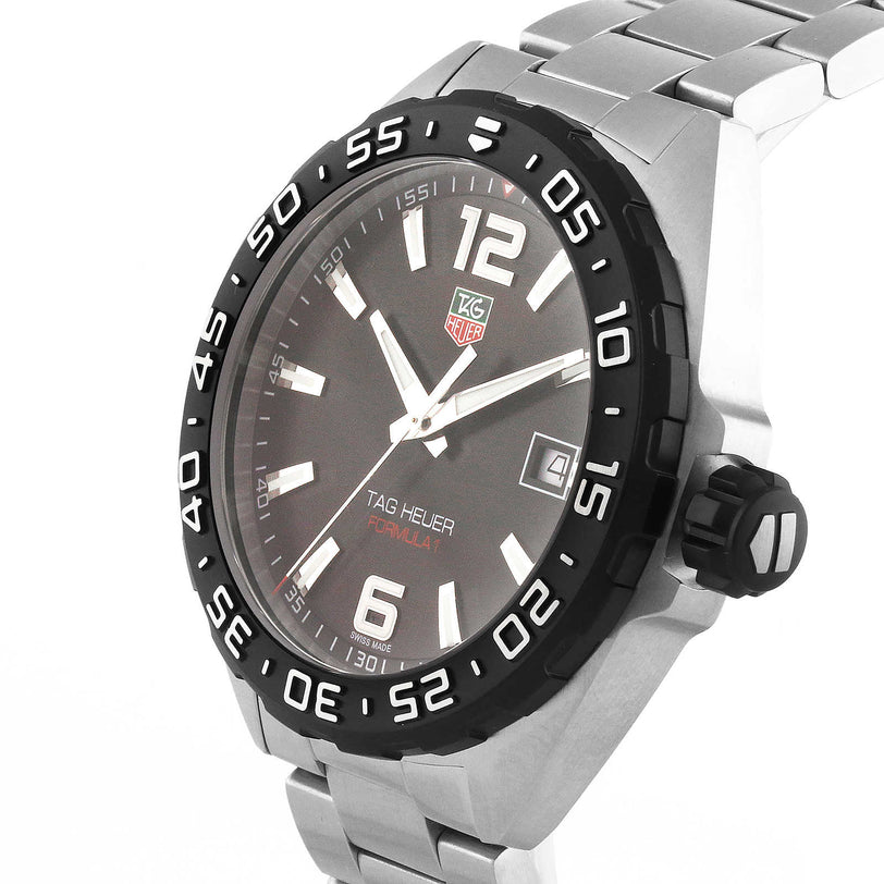 The TAG Heuer Formula 1 Date watch features a stainless steel case, black bezel, steel band, dark dial with date display, and large numerals at 6 and 12 o’clock.