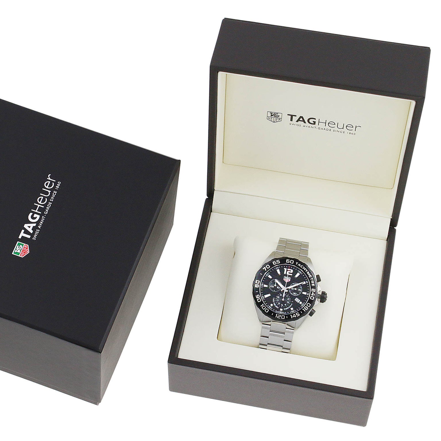 A TAG Heuer Formula 1 Chronograph with a black dial and silver metal band is shown in an open branded box beside a closed TAG Heuer box.