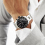A person in a light gray suit wears a TAG Heuer Formula 1 Chronograph wristwatch with a black face and tachymeter bezel.