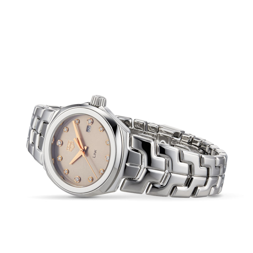 The TAG Heuer Link Date luxury silver watch features a metallic link band, round sunburst taupe dial, gold hour markers, and date display, shown angled on a white background.