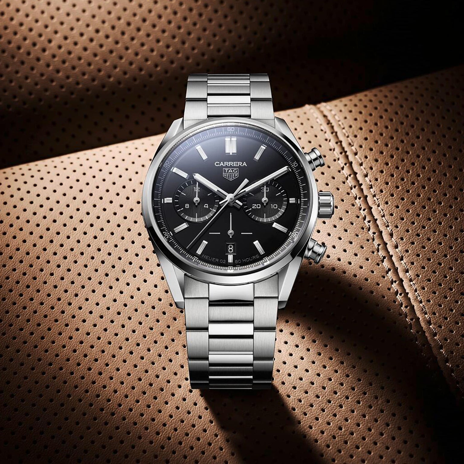 The TAG Heuer Carrera Chronograph, featuring a black dial and calibre Heuer 02 movement, is displayed on a perforated brown leather surface that reflects the brand’s motor-racing heritage.
