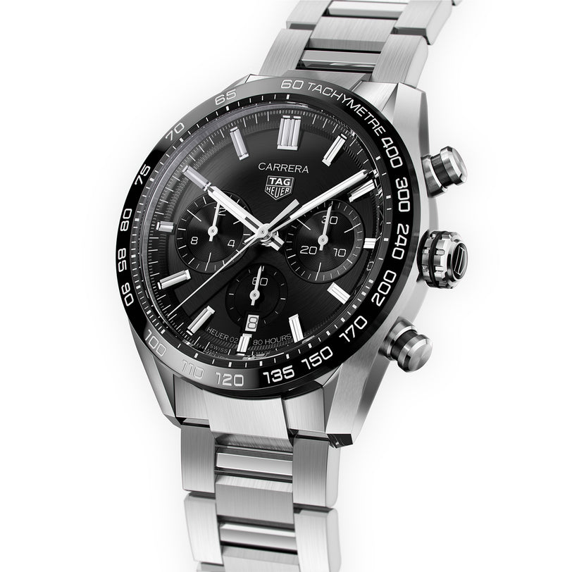 The TAG Heuer Carrera Chronograph features a silver case, black dial, three subdials, tachymeter bezel, Calibre 02 Automatic movement, and stainless steel bracelet, shown angled on a white background.