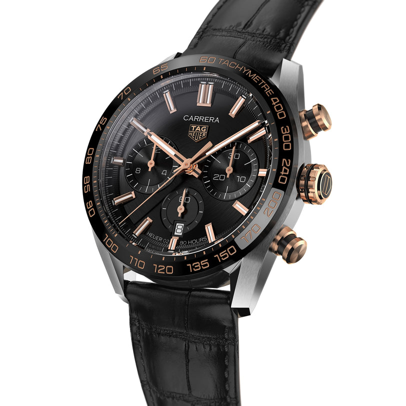 The TAG Heuer Carrera Chronograph features a black dial with gold accents, three subdials, a date window, and a black leather strap, powered by the Heuer 02 calibre—echoing TAG Heuer’s motor-racing heritage.
