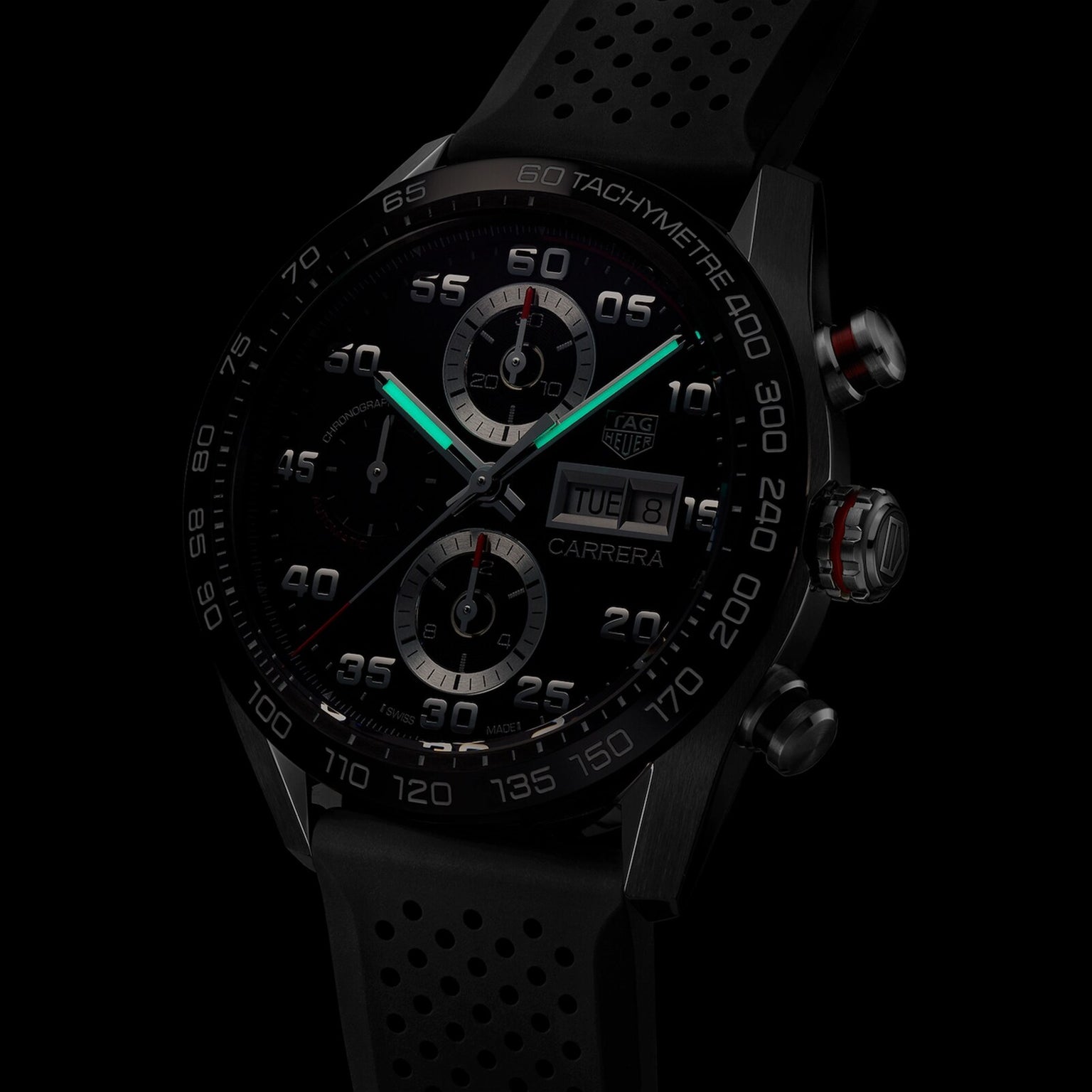Close-up of the TAG Heuer Carrera Chronograph, featuring a black dial, illuminated hands, tachymeter bezel, and black perforated rubber strap—powered for endurance.