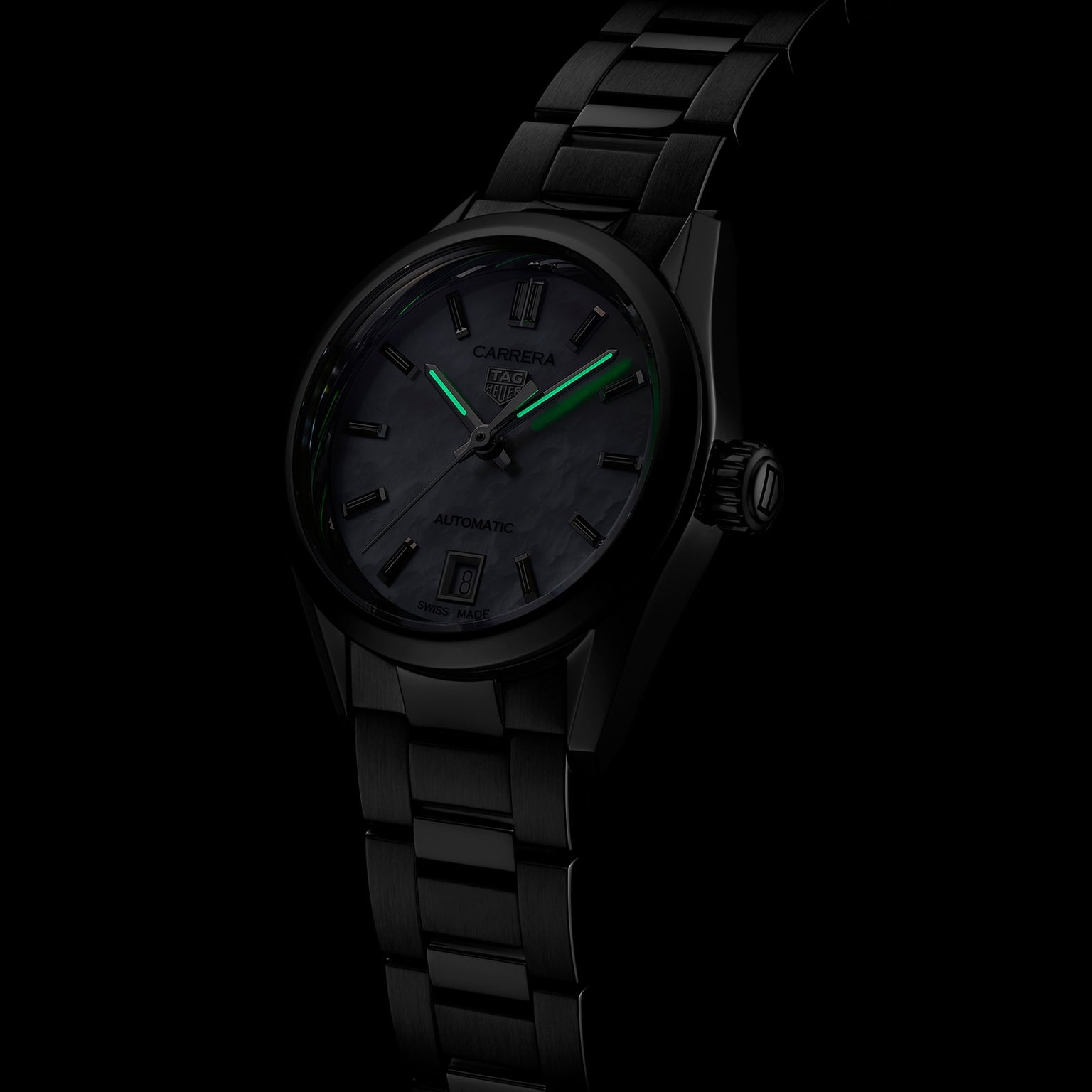 The TAG Heuer Carrera Date is a black luxury wristwatch with green glowing hands and markers, set against a dark background.