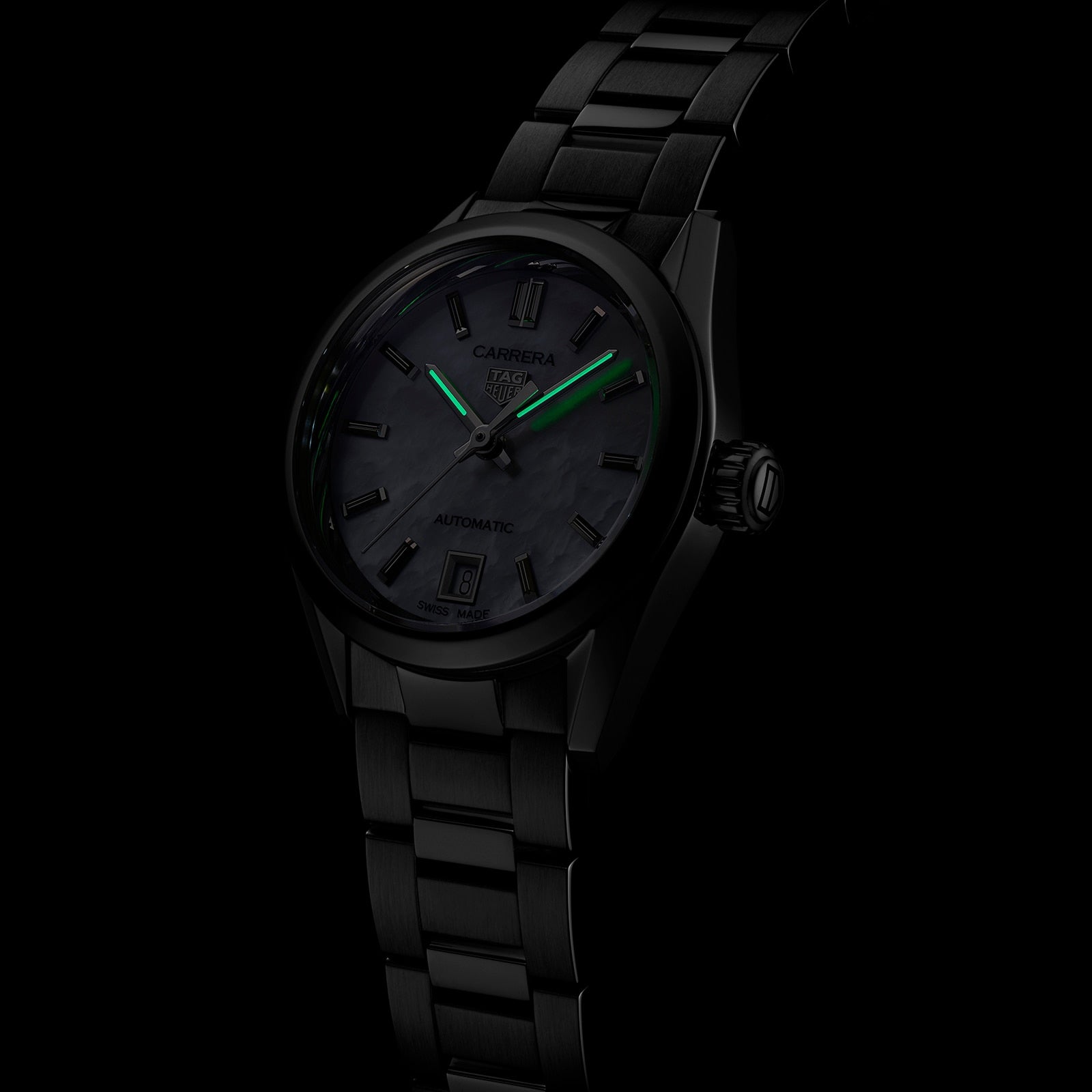 The TAG Heuer Carrera Date is a black luxury wristwatch with green glowing hands and markers, set against a dark background.