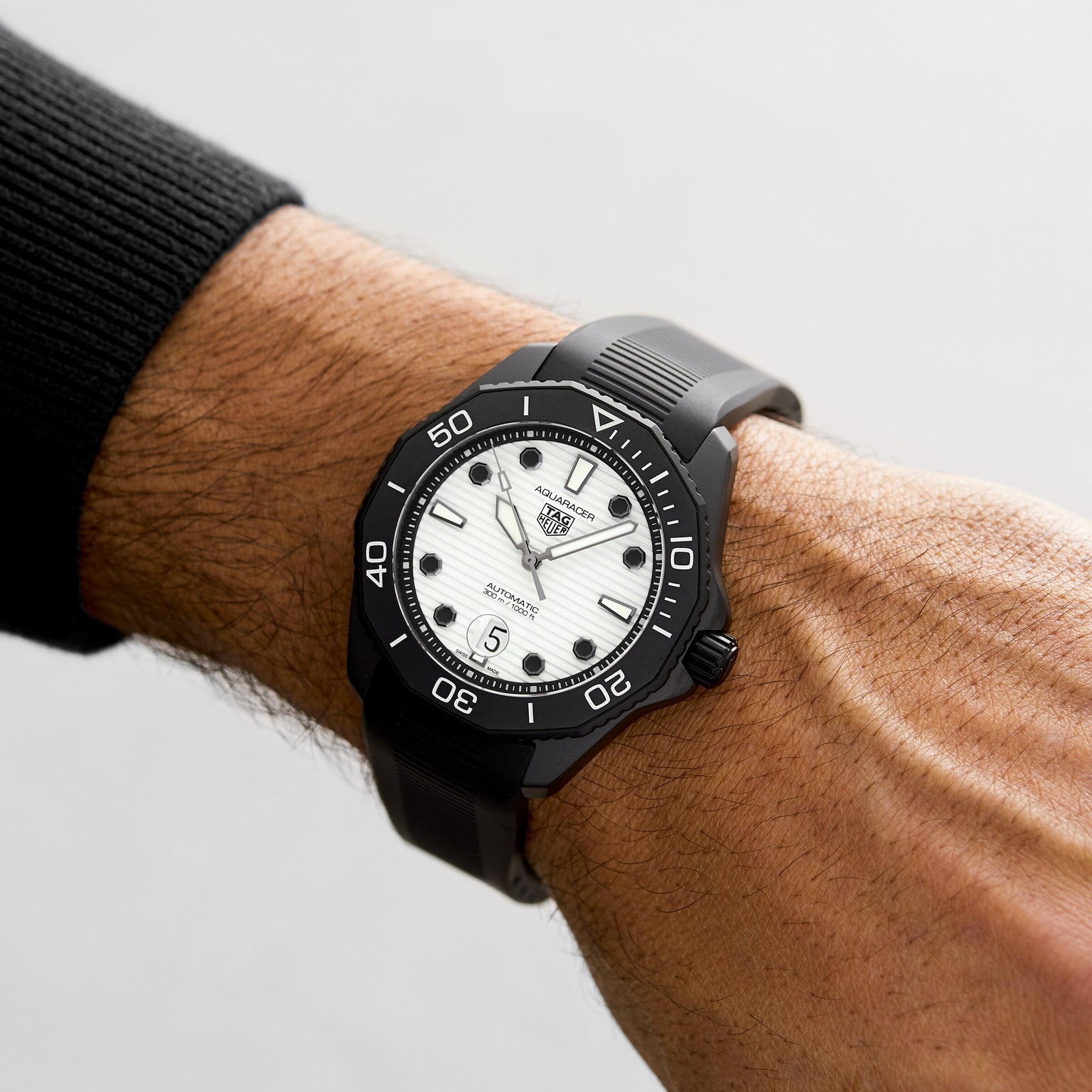 A persons wrist wearing a TAG Heuer Aquaracer Professional 300 Date dive watch with a white dial, black markers, date display, automatic movement, and black rubber strap.