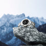 The TAG Heuer Aquaracer Professional 200, a silver sports watch with black dial and stainless steel case, is displayed on a gray rock against a backdrop of snow-capped mountains.