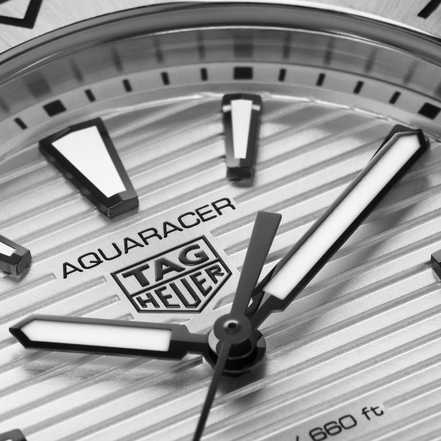 Close-up of a TAG Heuer Aquaracer Professional 200 watch face featuring a striped texture, bold luminous hour markers, stainless steel case, and partially visible hour and minute hands.