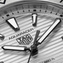 Close-up of a TAG Heuer Aquaracer Professional 200 watch face featuring a striped texture, bold luminous hour markers, stainless steel case, and partially visible hour and minute hands.